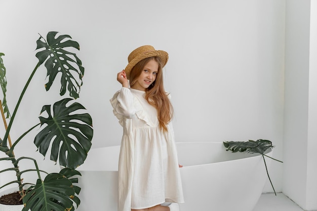 a girl in a white dress and a straw hat in a room with plants and a bathroom