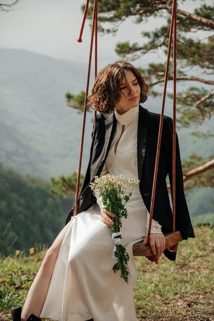 Girl in white dress swinging on a swing in the mountains