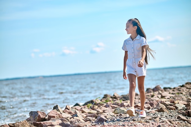 A girl in a white dress walking on a beach