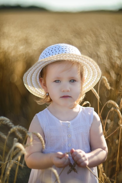 A girl in a white dress in a wheat field summer time children\
protection day