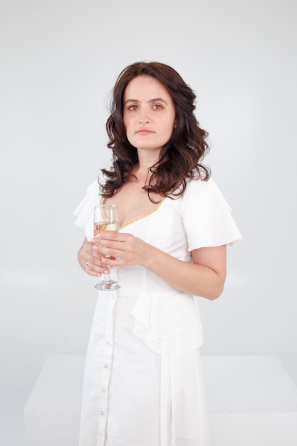 Girl in a white dress on a white background with a glass of champagne