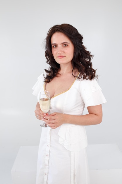 Girl in a white dress on a white background with a glass of champagne