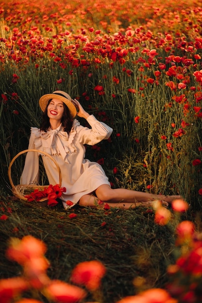 A girl in a white dress and with a basket of poppies is sitting on a poppy field