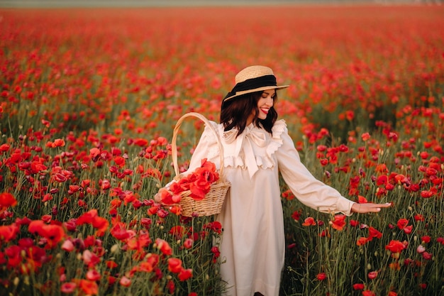 A girl in a white dress and with a basket of poppies walks through a poppy field