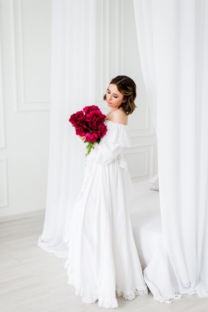 Ragazza in un abito bianco con un bouquet di peonie