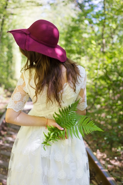 A girl in a white dress with cherry hat in woods