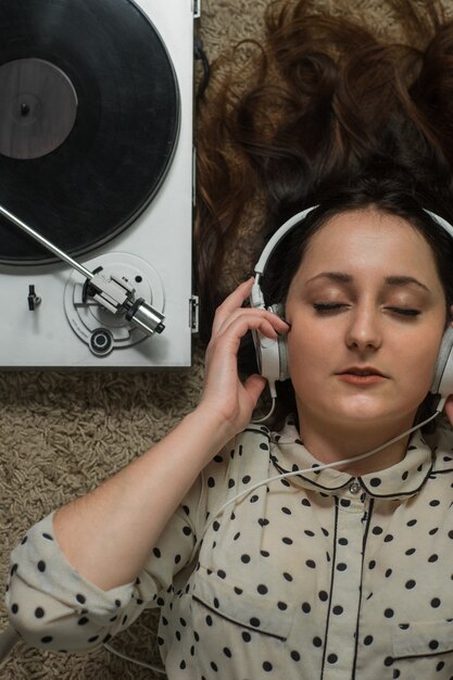 girl in white headphones on the floor listening to a turntable.