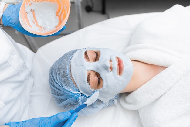 A girl in a white robe gets an alginate mask on her face.