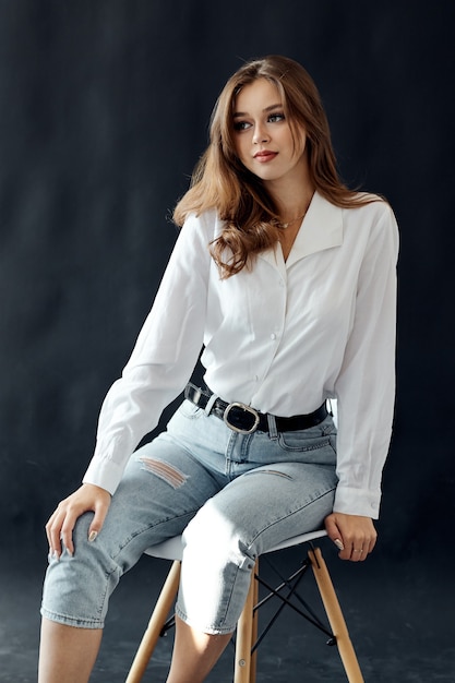 Girl in a white shirt on a dark background in jeans