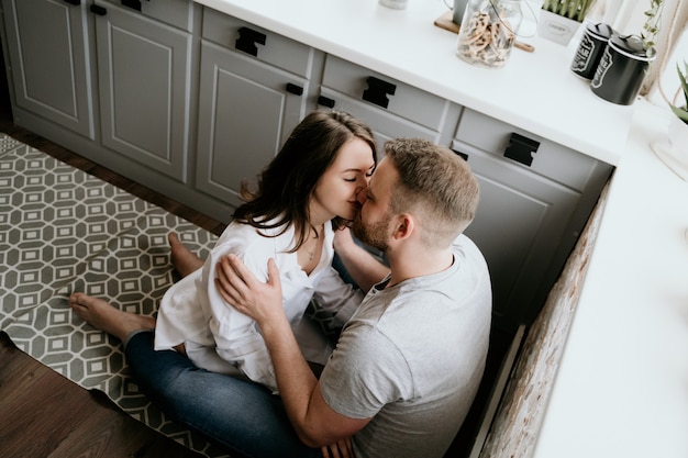 Girl in a white shirt and a guy in a gray t-shirt in the kitchen. kiss and hug