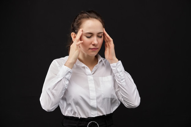 Girl in a white shirt hands hands massage the temple of the head on a black space.