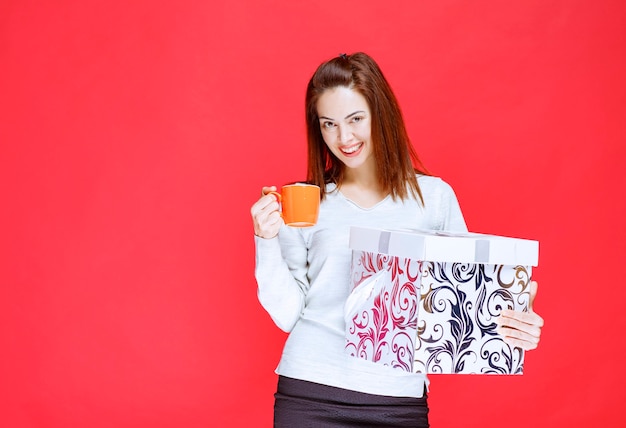 Girl in white shirt holding a printed gift box and having a cup of drink