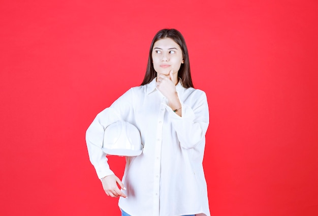 Girl in white shirt holding a white helmet and looks confused and thoughtful