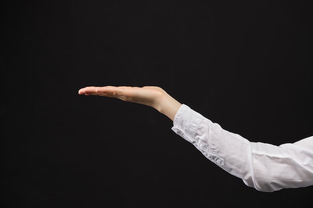 Girl in a white shirt holds an object in the palm of her hand on a black background.