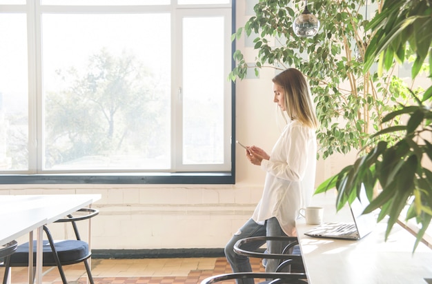 A girl in a white shirt is looking at smartphone between freelancer work.