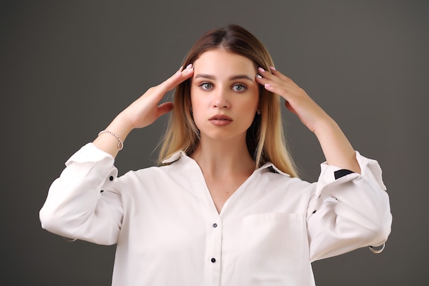 Ragazza in una camicia bianca in posa su uno sfondo grigio in studio.