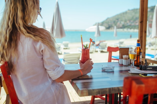 Girl in a white shirt sits with a cocktail in a restaurant near the sea