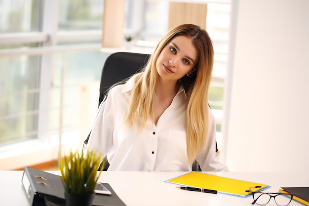 Foto ragazza in una camicia bianca seduta in ufficio, studente.