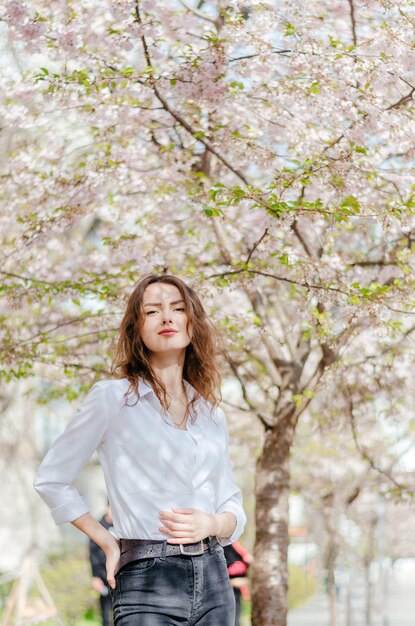 白いシャツを着た女の子が花の咲く桜の近くに立っています