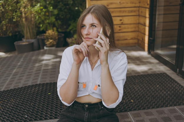 A girl in a white shirt in town talking on the phone