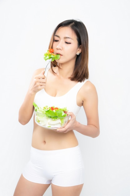 Girl in a white sport bra holds a salad bowl.