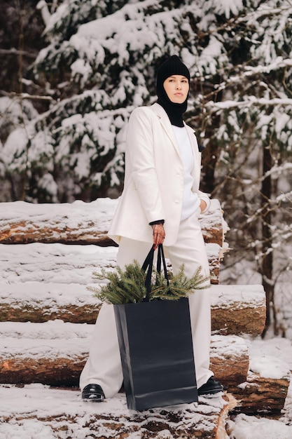 A girl in a white suit and balaclava with a package of Christmas trees in the winter forest on New Year's EveNew Year's concept