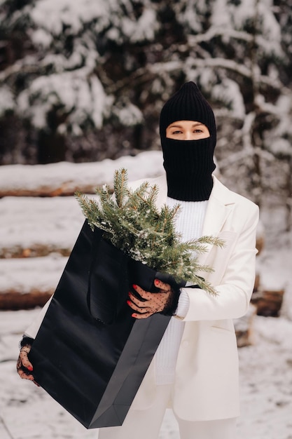 A girl in a white suit and balaclava with a package of Christmas trees in the winter forest on New Year's EveNew Year's concept