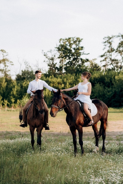 Девушка в белом сарафане и парень в белой рубашке на прогулке с коричневыми лошадьми в деревне