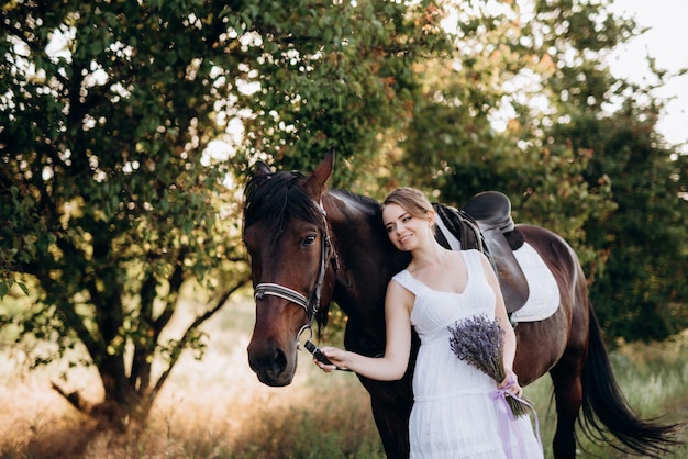 Girl in a white sundress on a walk with brown horses in the village