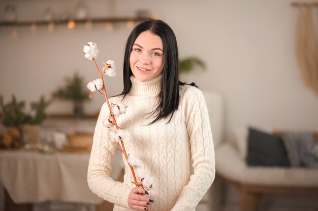 Girl in a white sweater dress with a cotton branch in a rustic style