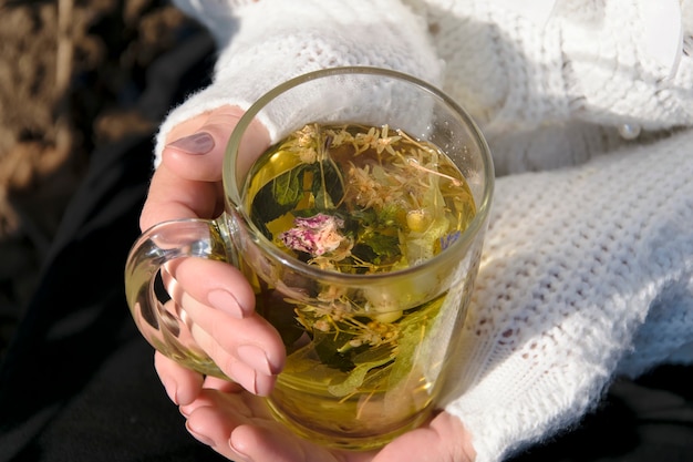 A girl in a white sweater is holding a glass cup with herbal tea