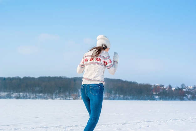 Девушка в белом свитере зимой бежит по заснеженному льду озера