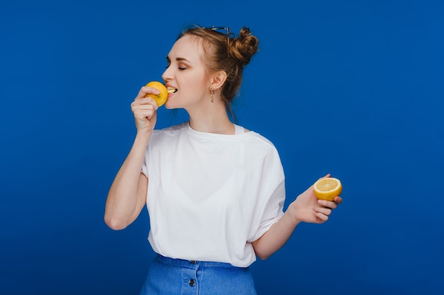 a girl in a white t-shirt bites a lemon