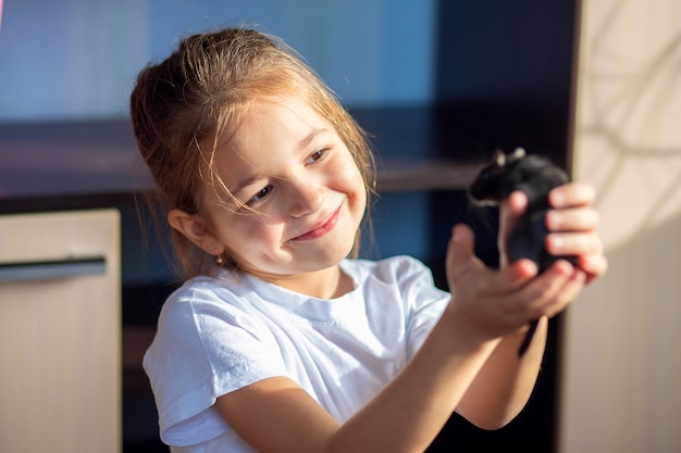 A girl in a white T-shirt holds a Mongolian gerbil in her hands and hugs her