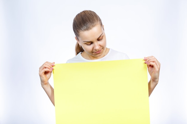 A girl in a white T-shirt is holding a yellow blank large sheet of banner.