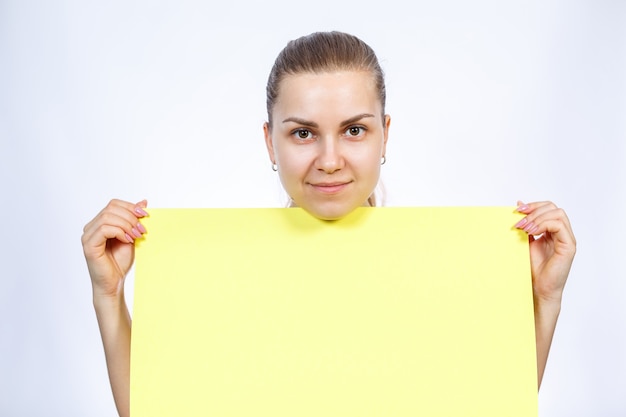 A girl in a white T-shirt is holding a yellow blank large sheet of banner.