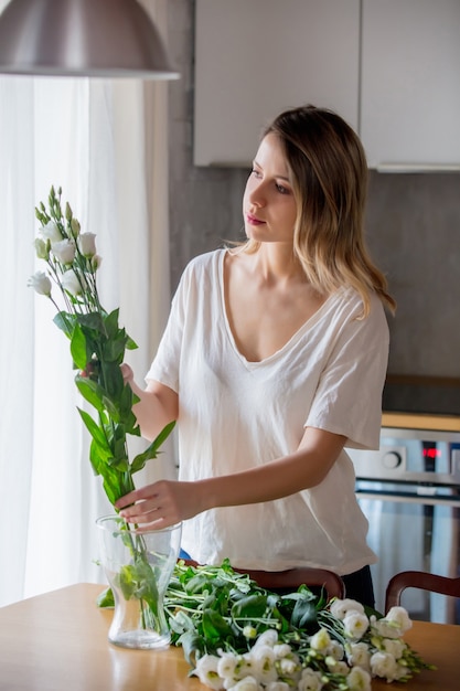 A girl in a white T-shirt is preparing a bouquet of white roses before putting them in a vase on the kitchen table. Lifestyle concept