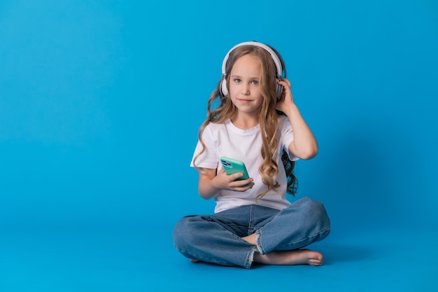 Ragazza con una maglietta bianca e jeans ascolta la musica tramite le cuffie su uno smartphone mentre è seduta