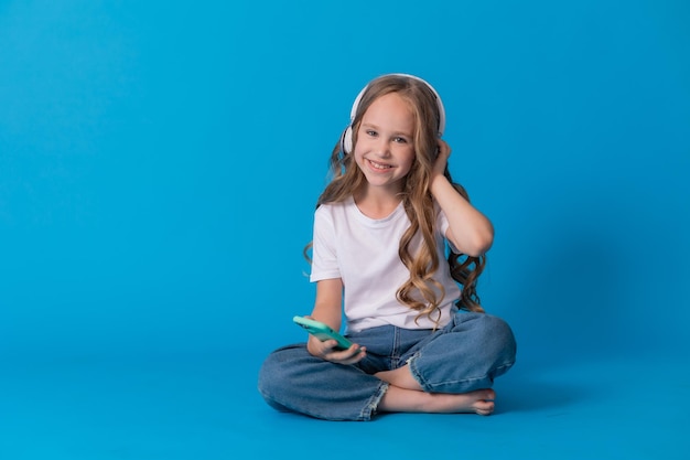 girl in a white T-shirt and jeans listens to music through headphones on a smartphone while sitting