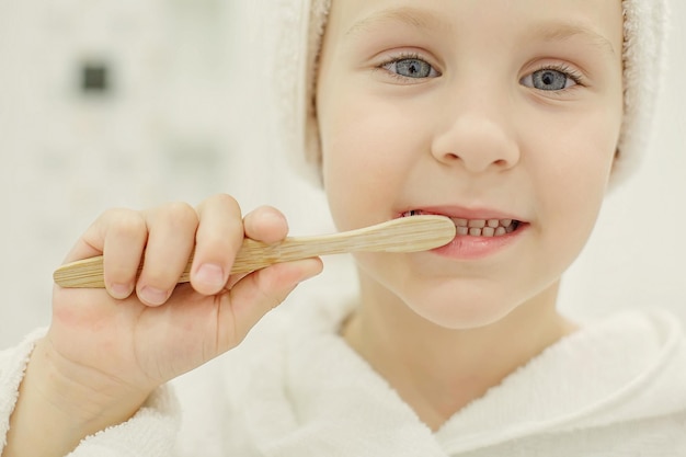 a girl in a white towel on her head and a white robe holds a wooden toothbrush