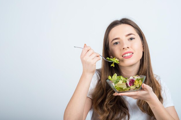 girl in a white tshirt holds a bowl of salad in her hands and eats