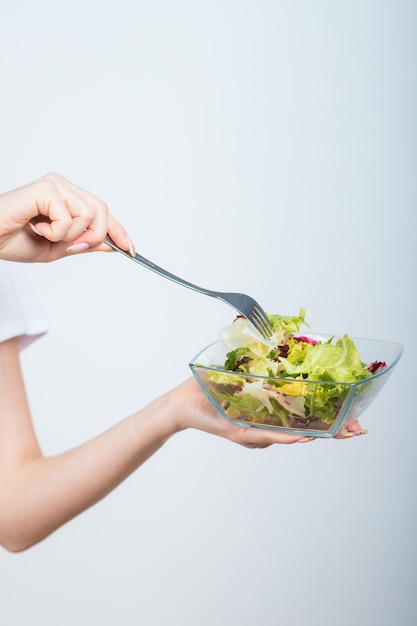 girl in a white tshirt holds a bowl of salad in her hands and eats