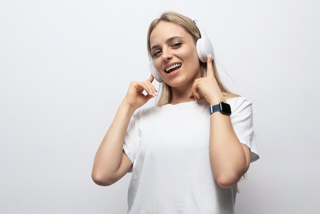 A girl in a white tshirt listens to music in wireless headphones on a white background with empty