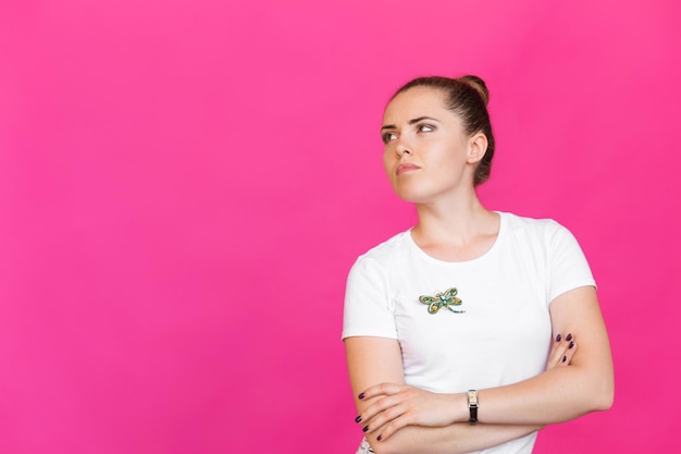 Girl in a white tshirt posing with a brooch shape of dragonfly with blue green gemstone imitation on pink background