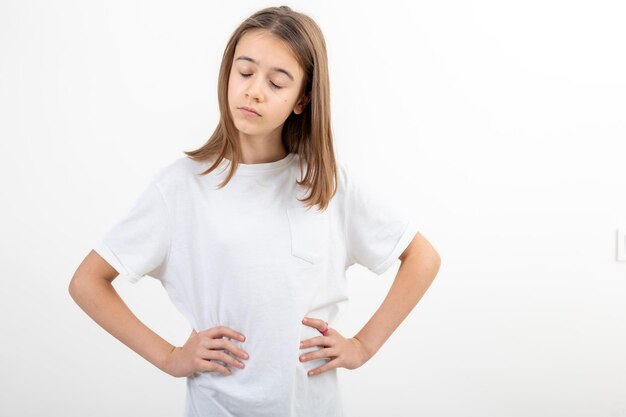 A girl in a white tshirt on a white background holds her hands on her waist