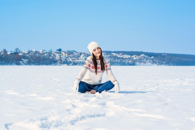 하얀 겨울 스웨터를 입은 소녀 눈 속에 다리를 꼬고 앉아 눈을 위로 던진다