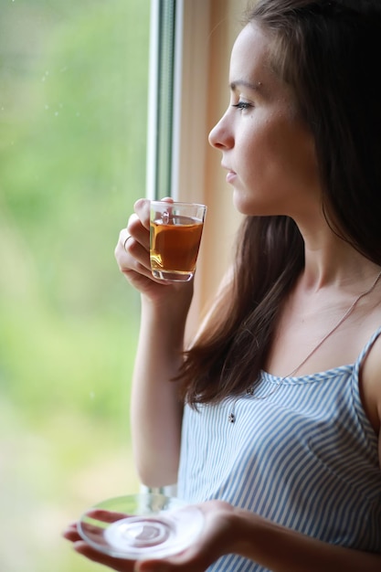 家の窓際の女の子が本を読んでお茶を飲む