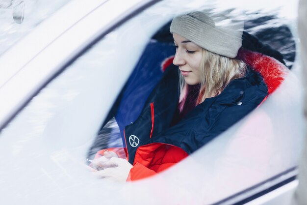 La ragazza con i vestiti invernali in macchina guarda il telefono