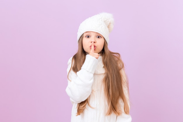 A girl in winter clothes and a white warm hat makes a gesture with her hands quieter.