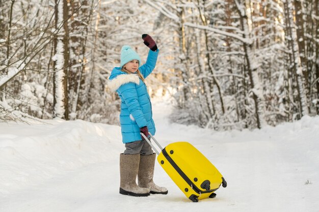 冬のフェルトブーツを履いた女の子が、凍るような雪の日にスーツケースを持って行く